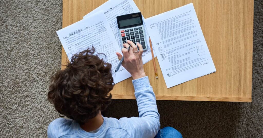 personne avec papiers et calculatrice sur une table en bois qui remplit déclaration fiscale 