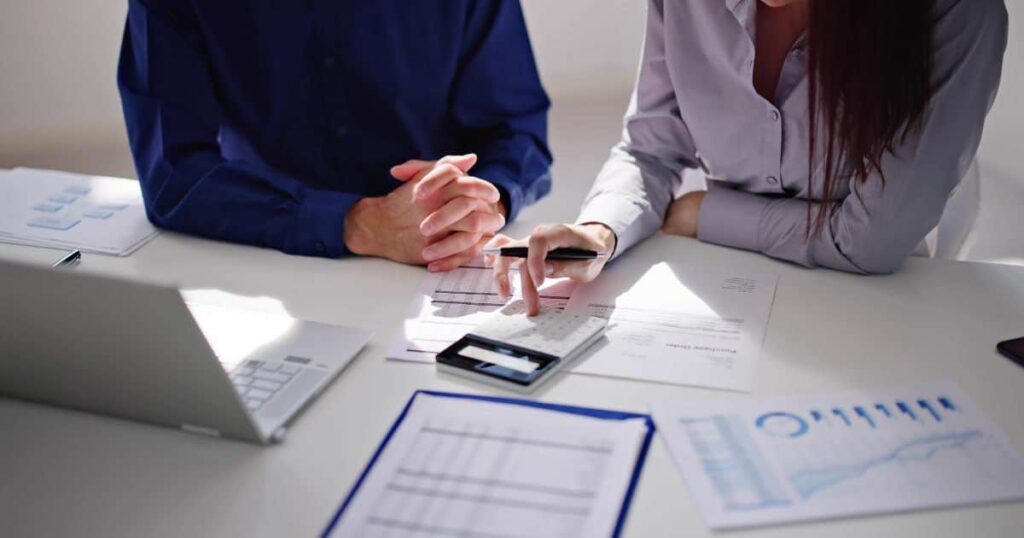 une femme et un homme en train de calculer sur un bureau blanc avec un ordinateur et des feuilles