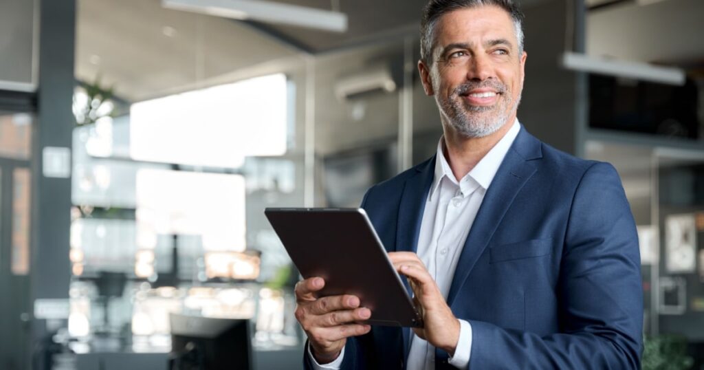 Un chef d'entreprise tient une tablette dans les mains et sourit en regardant au loin. 